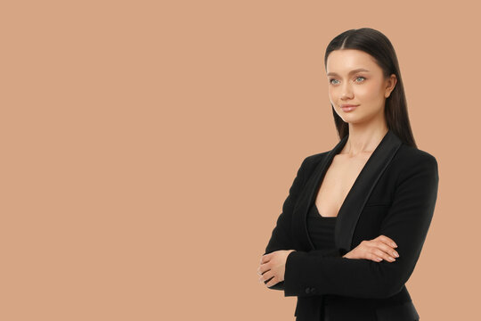 A woman poses in black attire with arms crossed in a plain space