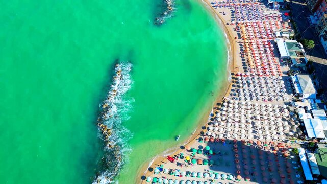 Amazing aerial pedestal up top-down bird's-eye shot from Porto Recanati, the Adriatic Sea waters coming into full view with breakwaters and waves, foam splashing on the beach with parasols and resorts