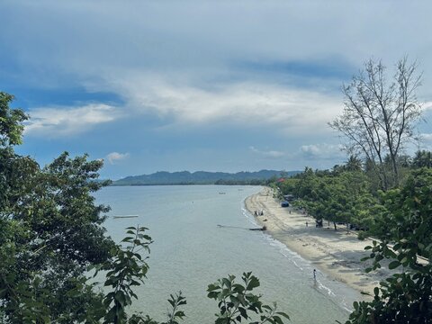Coastal Serenity: A tranquil beach scene with calm ocean waters gently lapping against a sandy shore, framed by lush green trees under a partly cloudy sky