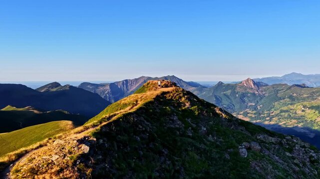 Aerial orbit follows winding ridge trail toward stone shelter revealing golden sunset over layered Pyrenees mountains at Col d'Aubisque