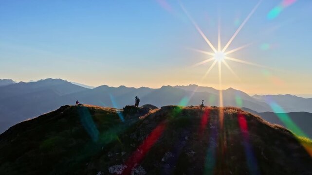 Aerial view shows tourists walking mountain ridge as sun sets in brilliant starburst above layered peaks at Col d'Aubisque