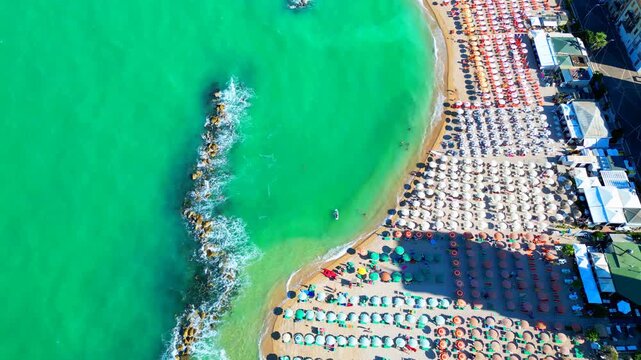 Beautiful aerial top-down bird's-eye pedestal down tilt-up shot from Porto Recanati, camera looking downwards to the Adriatic Sea, breakwater and beach with parasols, to encompass the beach with sky
