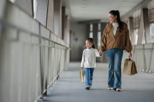 happy mother and child girl with shopping bag walking on footbridge in city