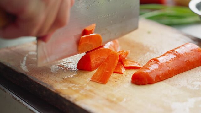 Thinly sliced carrots with Chinese kitchen knife on wooden cutting board
