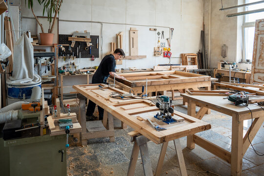 Small business woodworking studio providing complete vintage furniture reconstruction service, professional craftsman working on restoring of old wooden window frame at workbench in carpentry workshop