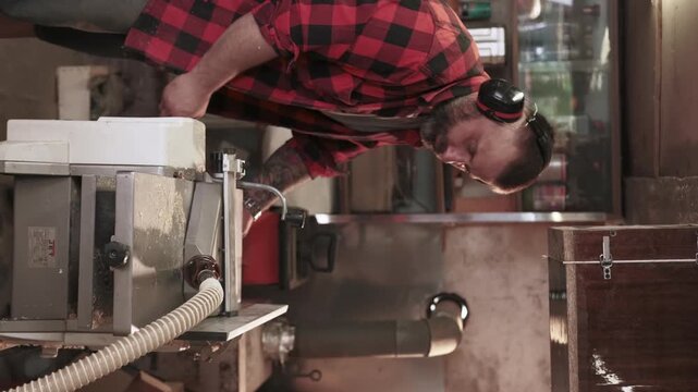 Vertical video. Carpenter work. Furniture making. Man with ear protectors processing wood on thickness planer with dust collection hose.