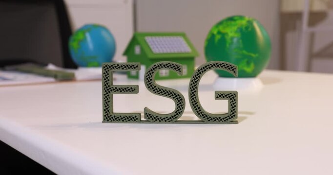 Green esg letters on a desk with globes and a small house, sustainable business and environmental responsibility.
