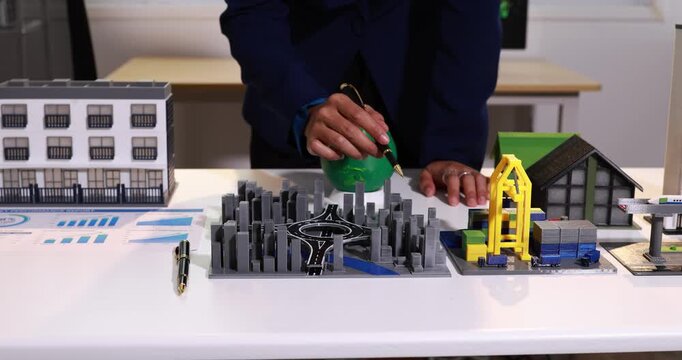 Businessperson working on an architectural city model with buildings, charts, and housing design on a desk