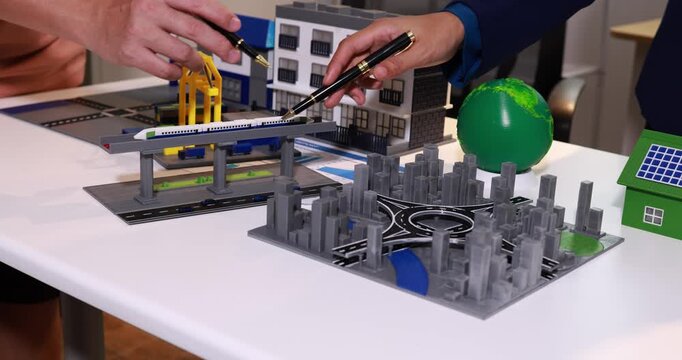 Hands examining a miniature city model with roads, buildings, a bridge and solar house on a table, urban planning, construction and smart city design.