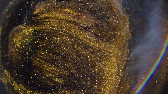 Blur glitter splash. Liquid spill. Defocused golden purple blue color paint sparkling rainbow on abstract acrylic light background.