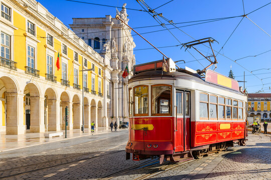A classic red-and-white heritage tram rolls past the majestic Arco da Rua Augusta and grand yellow arcades of Pra&ccedil;a do Com&eacute;rcio in the historic downtown core of Lisbon, Portugal.