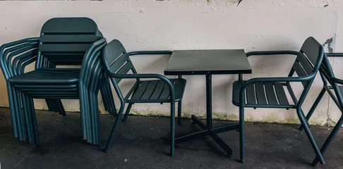 Fotobehang Horeca Stacked outdoor cafe chairs and a table against a white wall  © ArikEkaSatya