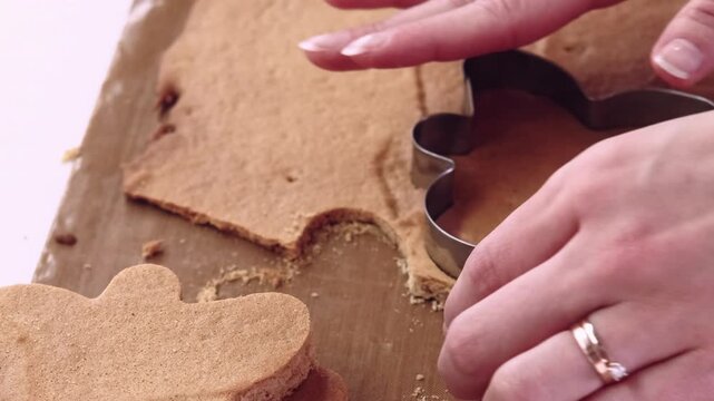 Dessert baking. Cookie making. Confectioner hand cut traditional gingerbread man shape treat from sweet dough crust sheet on brown mat.