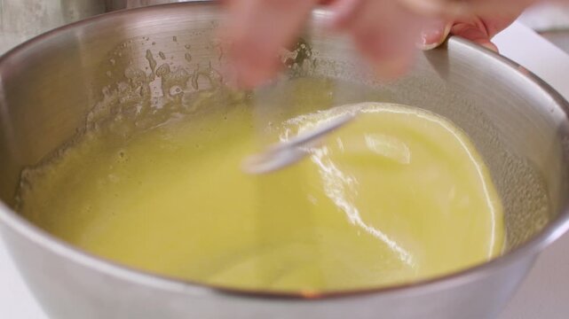 Cooking meal. Whisking process. Chef hand stirring yellow frothy liquid baking ingredient in stainless steel bowl with spring tool.