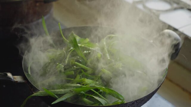 Use chopsticks to quickly stir-fry water spinach in a wok on the stove