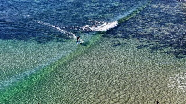 Aerial View of Stand Up Paddleboarder Surfing Clear Turquoise Wave