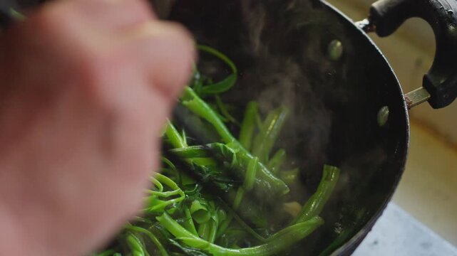 Close-up of green water spinach stir-fried in a hot iron pot in the kitchen