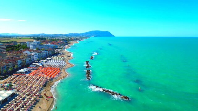 Ecstastic aerial push-in truck left pan left shot of Porto Recanati, from a view of the vast Adriatic Sea with Mount Conero in the distance, to flying above the beach with parasols, resorts, buildings
