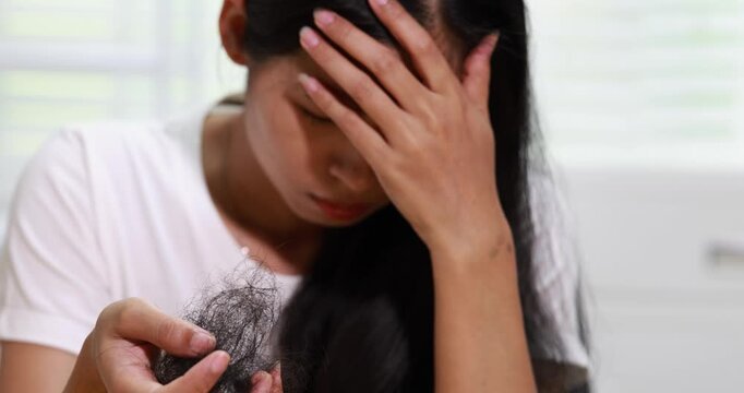 Worried young woman examining a clump of hair, concern about hair loss and thinning while sitting indoors.