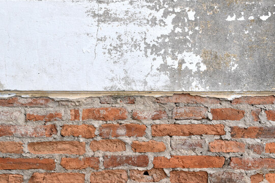 old weathered wall with peeling plaster revealing red brick layers