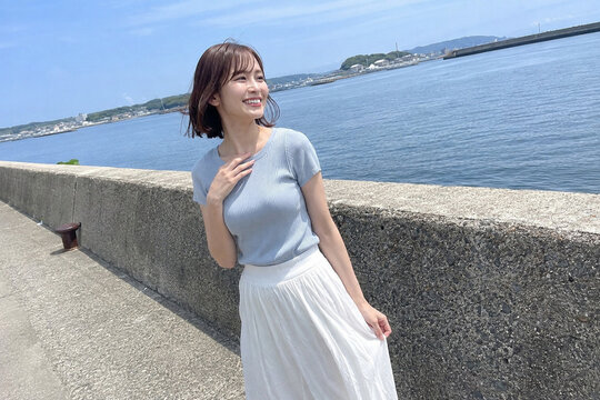 海沿いの防波堤で水色トップスを着た笑顔の女性