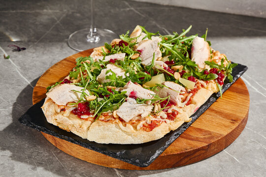 Turkey and arugula Roman pizza with juicy sliced poultry, red berries, pear and crunchy nuts on a wooden serving board