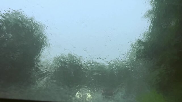 Rain on the windshield as the car drives through the city, heading towards oncoming vehicles with their headlights on.