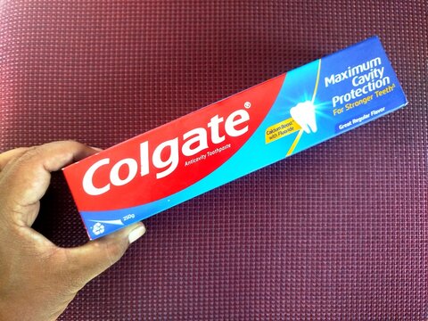 KUALA TERENGGANU MALAYSIA- AUGUST 06. 2026: Person holding a 250g box of Colgate Maximum Cavity Protection toothpaste with Great Regular Flavor against a red textured fabric background.