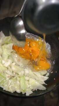 Cooking Thai food video showing preparation of stir fried flat rice noodles with pork. Cooking over high heat in wok with scrambled eggs, fresh cabbage, soy sauce, and chili flakes.
