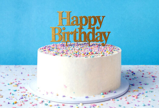 Delicious white birthday cake with colorful sprinkles and happy birthday topper on display
