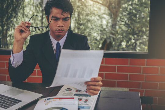 Tired businessman taking off glasses with eye pain during working and reading paperwork in office. Selected focus