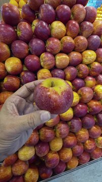 A hand holding red Apple while shopping in a supermarket