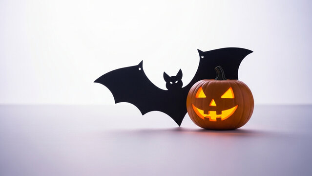An illuminated jack-o-lantern sits beside a dark paper silhouette representing a flying creature during the festive autumn period to celebrate the annual spooky night of traditional tricking
