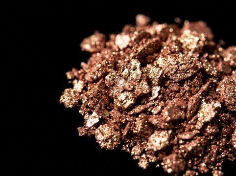 Pile of raw copper ore nuggets and metallic bronze flakes on black background