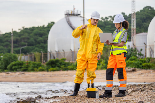 Environmental scientists in hazmat suit and safety gear testing water quality at industrial coastal area, Researchers collecting water sample analyzing pollution and environment safety with laptop