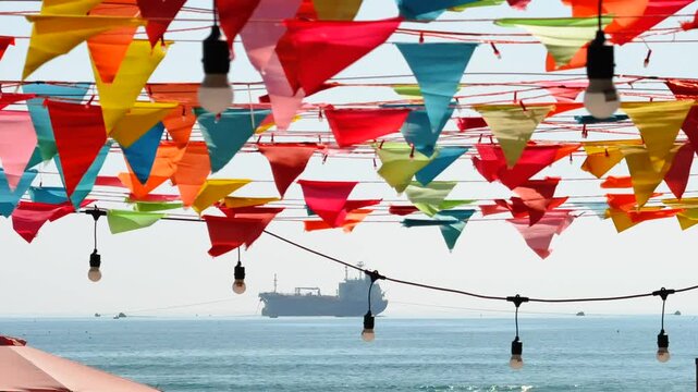 Close up of Colorful bunting pennant flags strung over seaside beach with big ship anchored in the horizon
