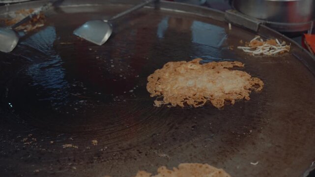 Street food chef frying crispy seafood omelet with mussels and shrimp on flat hot pan.