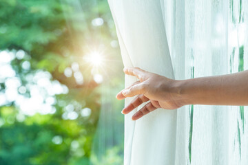 Obraz premium woman's hand She opened the curtains on the window. There was morning light through the window in her room, looking at the view of the mountains and trees as the sun rose. 