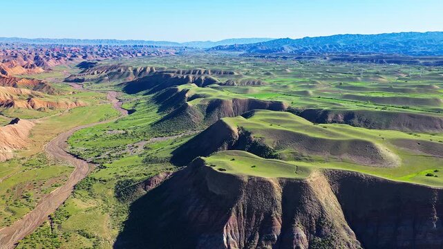 Aerial view of a majestic canyon with a winding riverbed and green grassy valleys along the S101 highway in Xinjiang, China.