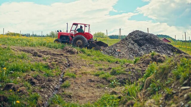 A Ferguson 35 Tractor With A Shovel Attachment Performs Loading Work Outdoors In A Rural Agricultural Area. Wide Shot