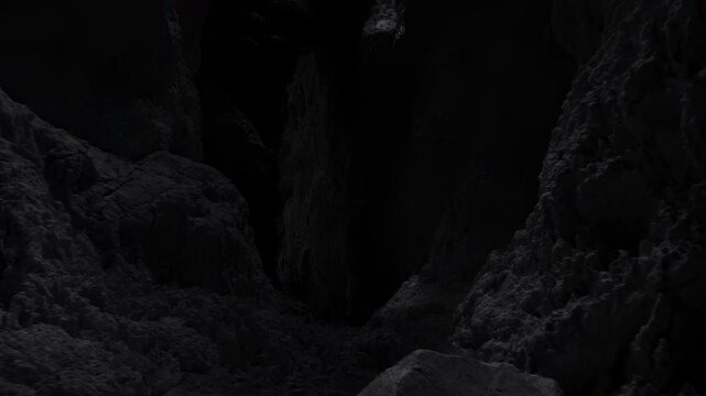 Dark limestone cave interior with narrow chasm, steep textured walls, rocky floor, deep shadow, rough mineral surfaces, moody contrast, and recessed viewpoint, with cave, limestone, chasm, dark detail