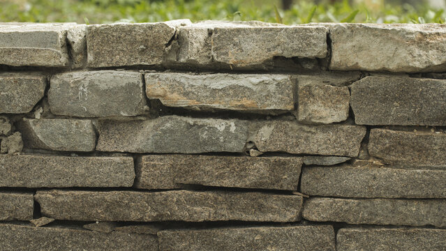 Detailed close-up of a stacked natural granite stone wall with a rough, uneven surface texture, natural background.