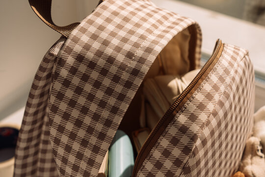 Open gingham backpack filled with school supplies in warm natural sunlight.