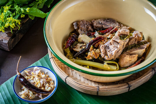 Traditional Northern Thai Jor Pak Kad soup with pork and mustard greens in a vintage enamel bowl on banana leaf. Authentic local dish with sour tamarind, herbs, and fried chili. 