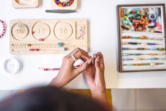 Asian woman making handmade beaded jewelry in creative workspace for artisan craft and small business creative entrepreneurship