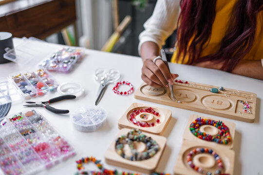 Asian woman making handmade beaded jewelry in creative workspace for artisan craft and small business creative entrepreneurship