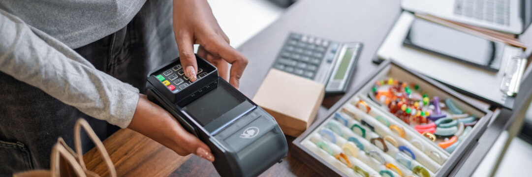Woman accepting cashless payment with EDC terminal at small business retail store during customer purchase.