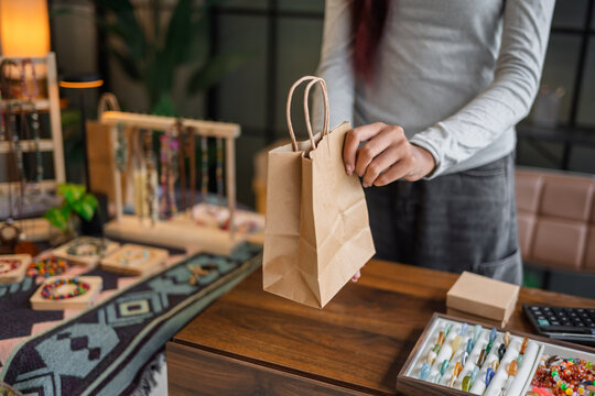 Woman packing customer purchase into paper bag for small business with sustainable packaging and eco friendly retail Green business.