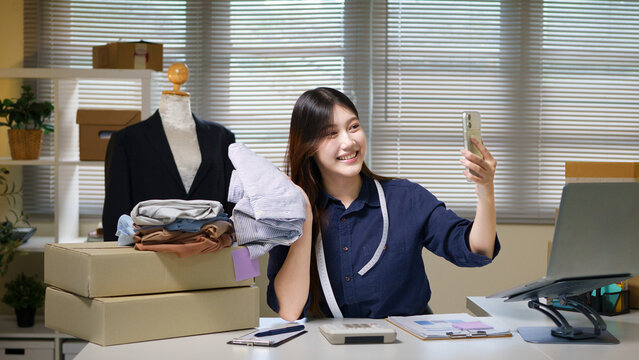 Young Asian Woman Fashion Entrepreneur Taking Selfie with Clothes for Online Store Social Media
