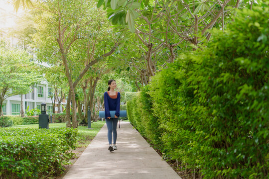 Asian Gen Z woman carrying yoga mat walking to park for wellness healthy lifestyle mindfulness and outdoor exercise